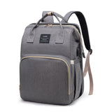 Charcoal gray mommy diaper backpack with roomy front pocket, top handles, and side USB charging port, three-quarter front view.