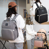 Lifestyle views of diaper backpack in gray and black—worn on back and attached to stroller handle.
