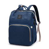 Navy blue mommy diaper backpack with top handles, padded straps, large front pocket, and side USB charging port, front view.