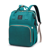 Teal mommy diaper backpack with top handles, padded shoulder straps, front zip pocket, and discreet side USB charging port, studio view.