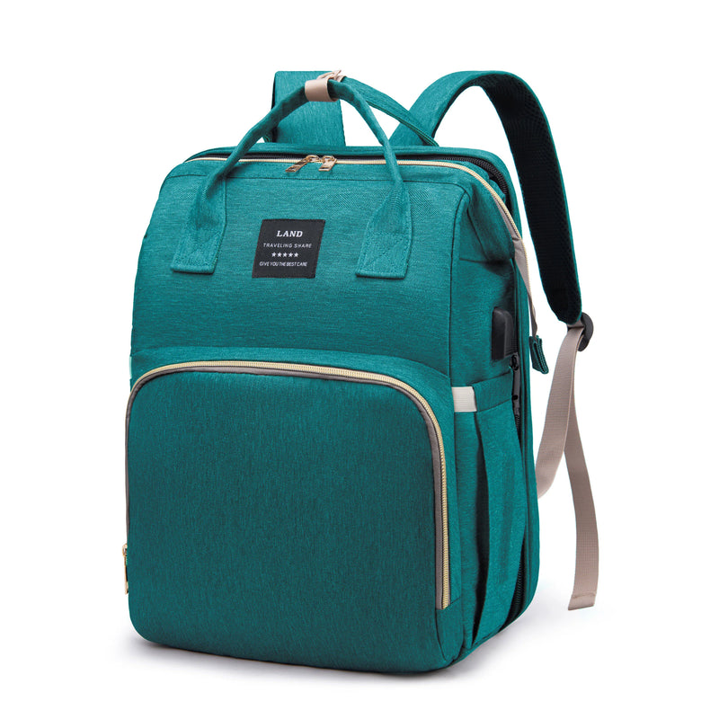 Teal mommy diaper backpack with top handles, padded shoulder straps, front zip pocket, and discreet side USB charging port, studio view.